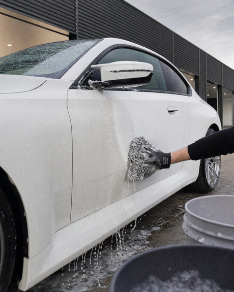 Daniel wäscht die Seite eines weißen BMW M2 mit dem Koch-Chemie Wash Mitt, eine Bahn schon glänzend, daneben noch staubig.