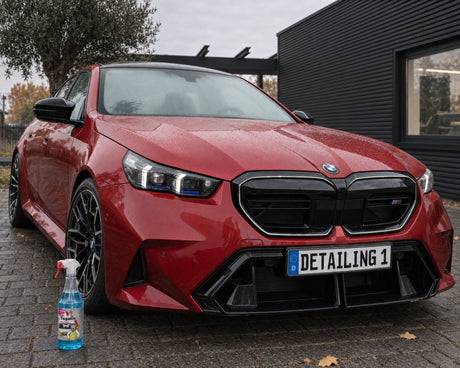 Tugalin Glas-Teufel davanti a una BMW M5 rossa con il parabrezza appannato — mostrato nell'articolo «L'auto si appanna dentro: perché un vetro pulito resta limpido più a lungo»