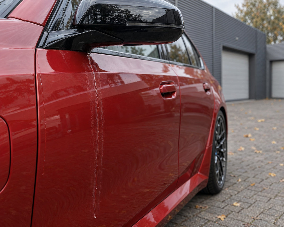 Detailing1 asciugare l'auto — l'acqua che cola dallo specchietto lascia aloni di calcare sulla portiera di una BMW M5 rossa