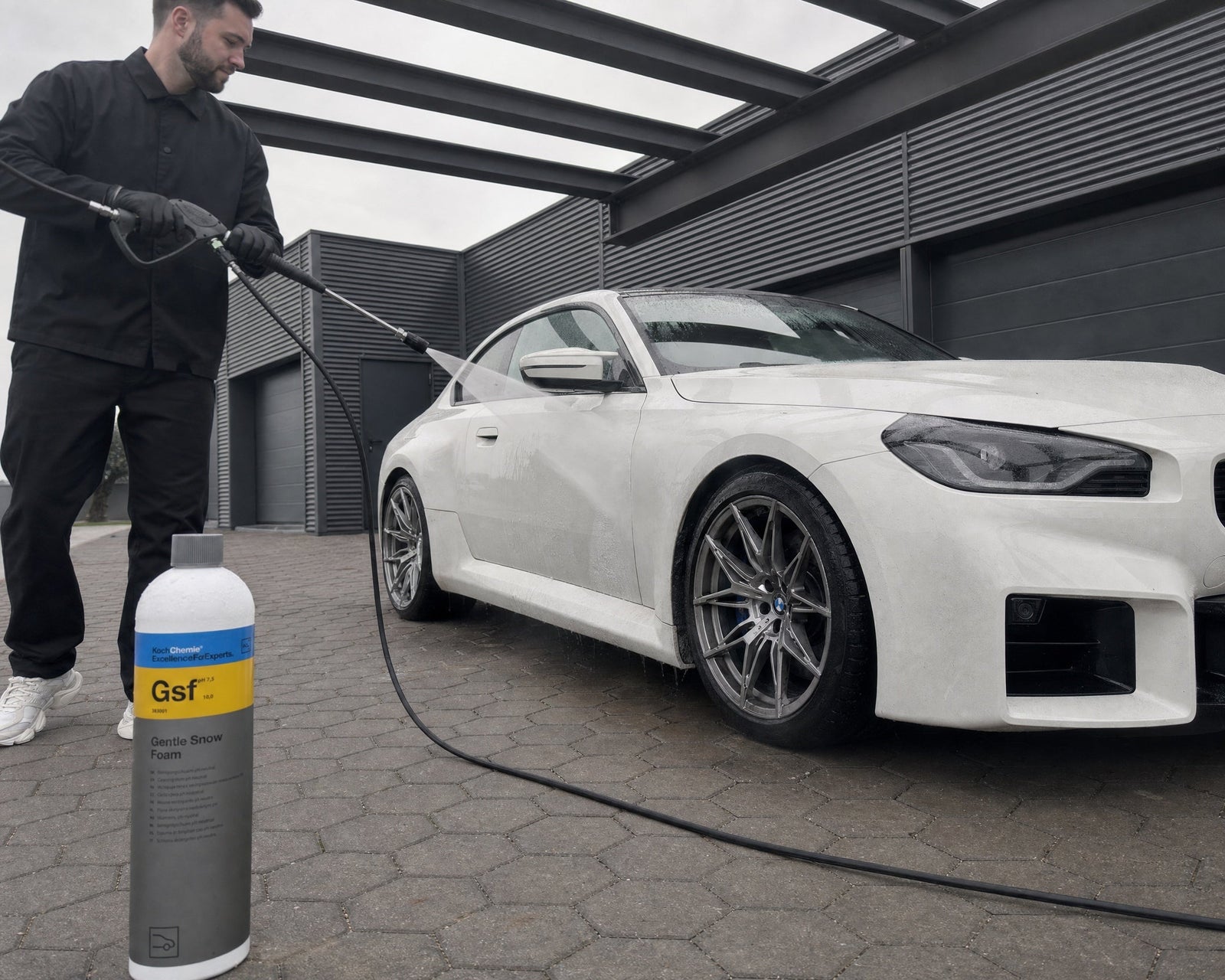 Daniel spült mit dem Hochdruckreiniger die Flanke eines weißen BMW M2 ab, die Koch-Chemie Gentle Snow Foam Flasche steht auf dem Pflaster — gezeigt im Artikel „Auto mit Hochdruckreiniger waschen: Düse, Abstand und Druck