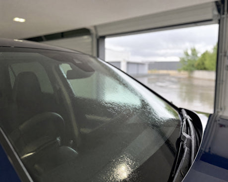 Regen läuft als flacher Wasserfilm über die Windschutzscheibe eines dunkelblauen Sportwagens — gezeigt im Artikel Scheibenversiegelung fürs Auto