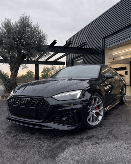Makellos glänzender schwarzer Audi RS 5 in der Halle, runde Wasserperlen auf der Haube, tiefe Spiegelung im Lack.