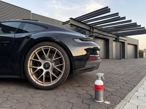 Koch-Chemie Magic Wheel Cleaner MWC 500ml auf Pflastersteinen neben verschmutzter Porsche-Felge — Werkstatt-Szene